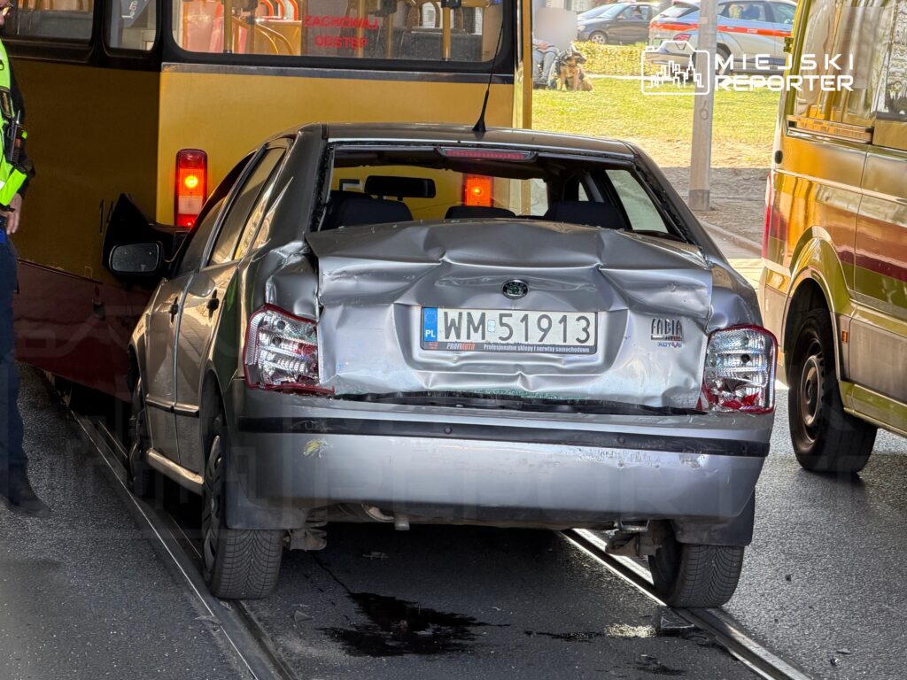 Zderzenie samochodu osobowego z autobusem, uszkodzona tylna część pojazdu, w tle policjant i karetkę.