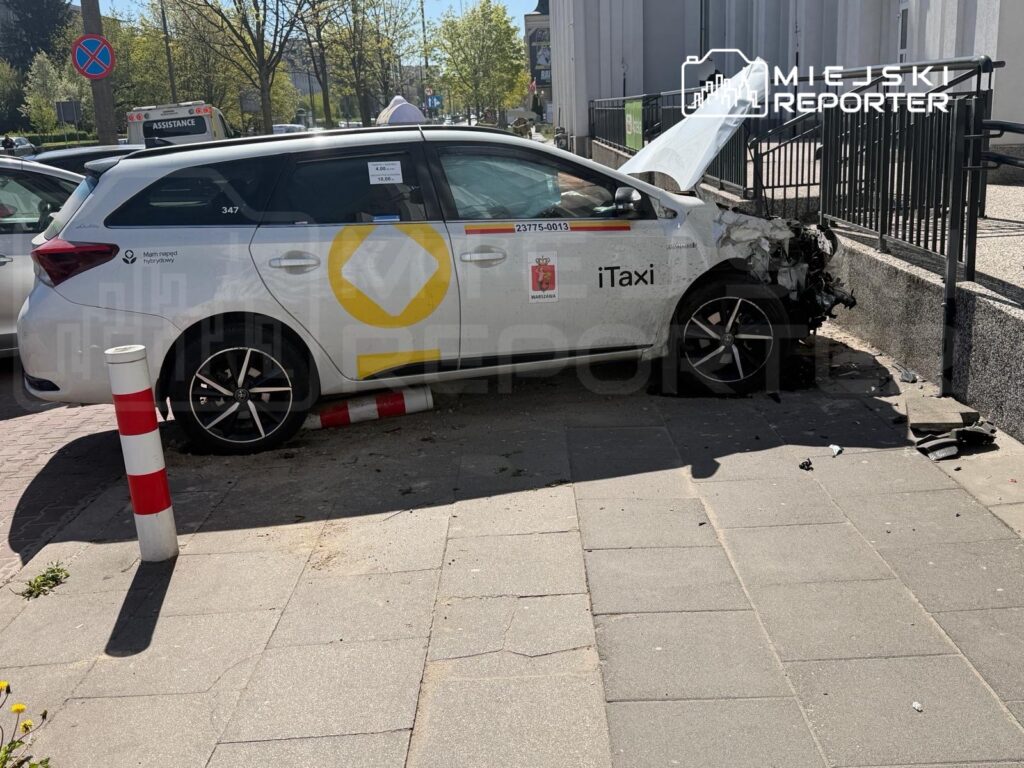 Uszkodzony samochód dostawczy iTaxi zatrzymany na chodniku, z przodu wgnieciony w barierkę.