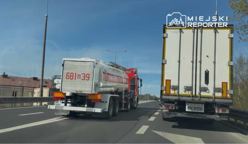 Czerwony samochód ciężarowy z cysterną wyprzedza biały pojazd dostawczy na drodze w słoneczny dzień.