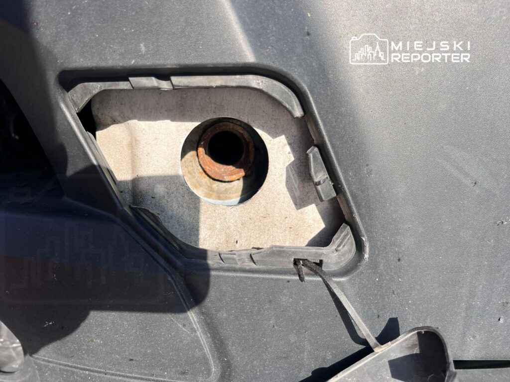 Widok na otwór w obudowie, w którym widać zardzewiałą rurkę. W tle czarna powierzchnia obudowy.