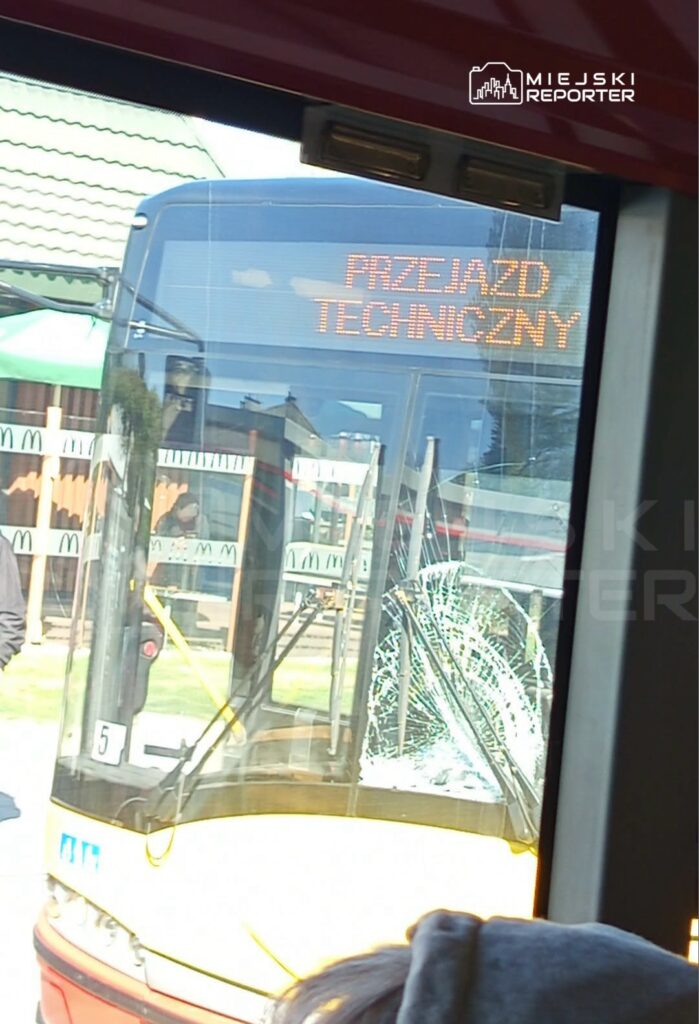 Autobus z wyświetlaczem informującym o "PRZEJAZD TECHNICZNY" oraz uszkodzoną szybą stoi na przystanku obok restauracji fast food.