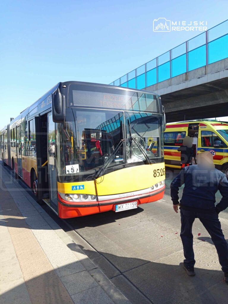Autobus komunikacji miejskiej zatrzymany na przystanku, obok pracownik w mundurze kontrolując sytuację.