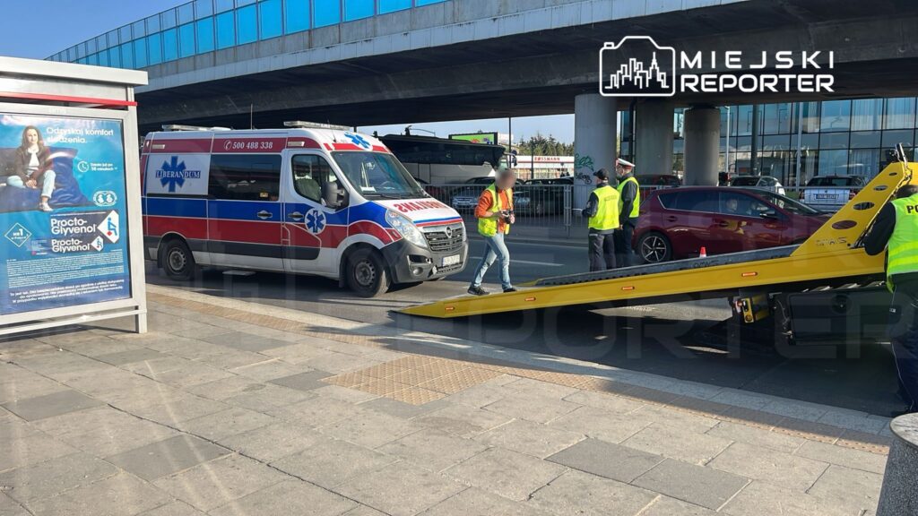 Zespół ratunkowy obsługuje zdarzenie drogowe przy przystanku, obok karetki i lawety.