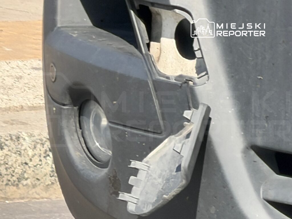 Zbliżenie na uszkodzoną osłonę reflektora w przednim zderzaku samochodu zaparkowanego na ulicy.