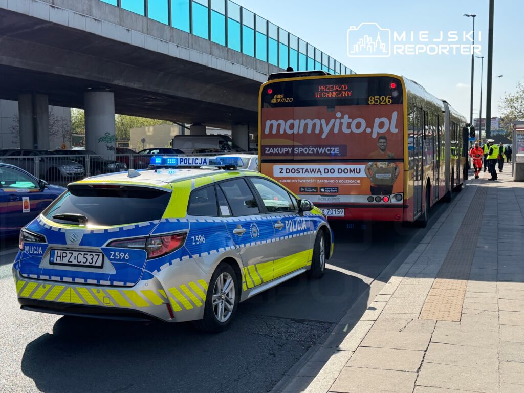 Radiowóz policyjny z włączonymi sygnałami świetlnymi stoi obok przystanku autobusowego, gdzie zatrzymał się autobus.