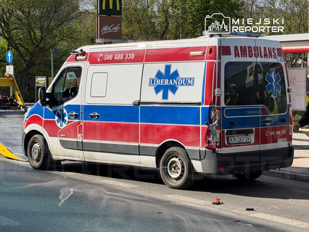 Karetka pogotowia w kolorze czerwonym i niebieskim zatrzymana przy McDonald's, z widocznym numerem telefonu i logo firmy.