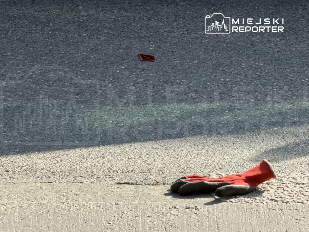 Czerwony rękawice robocze leżą na asfalcie obok małego, czerwonego przedmiotu.