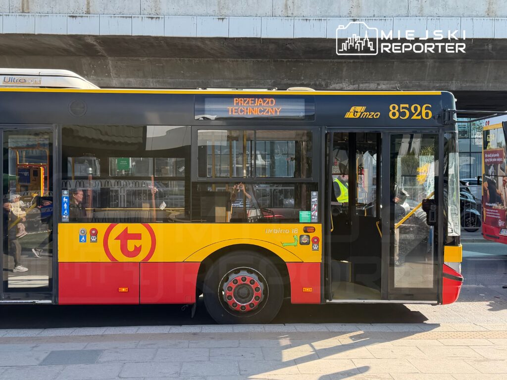 Autobus komunikacji miejskiej z oznaczeniem „Przejazd techniczny” zatrzymany na przystanku, w tle ruch uliczny.