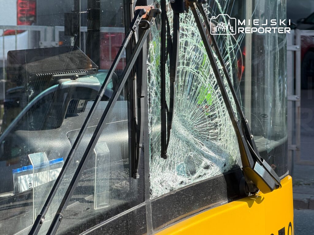 Uszkodzona szyba przednia żółtego autobusu miejskiego z widocznymi pęknięciami, stojącego na ulicy.