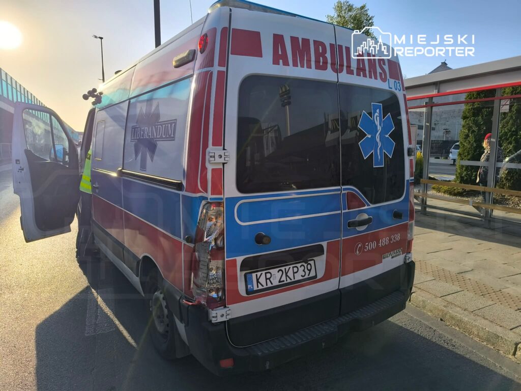 Karetką pogotowia z otwartymi drzwiami podjeżdża do przystanku, w tle widoczny zachód słońca.