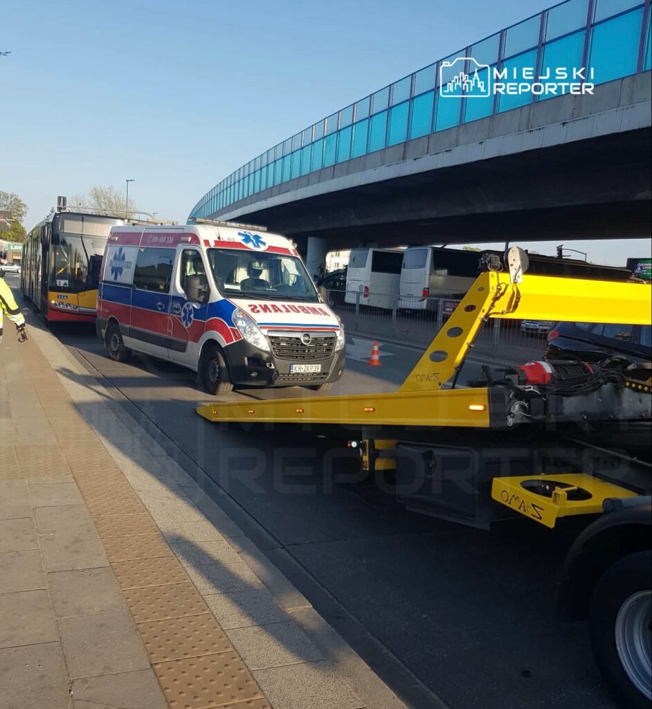 Karetka pogotowia przejeżdża obok tramwaju, a w tle widoczna jest żółta laweta na ulicy.