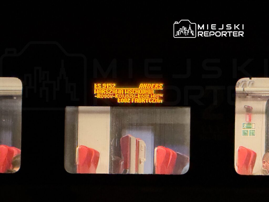 Pociąg z wyświetlaczem informacyjnym pokazującym trasę Warszawa Wschodnia - Łódź Fabryczna, w tle widoczne czerwone siedzenia.