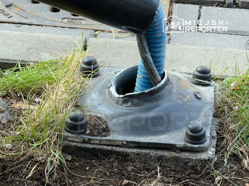 Nieczynna instalacja z niebieską rurą wychodzącą z metalowej podstawy, otoczona trawą i ziemią.