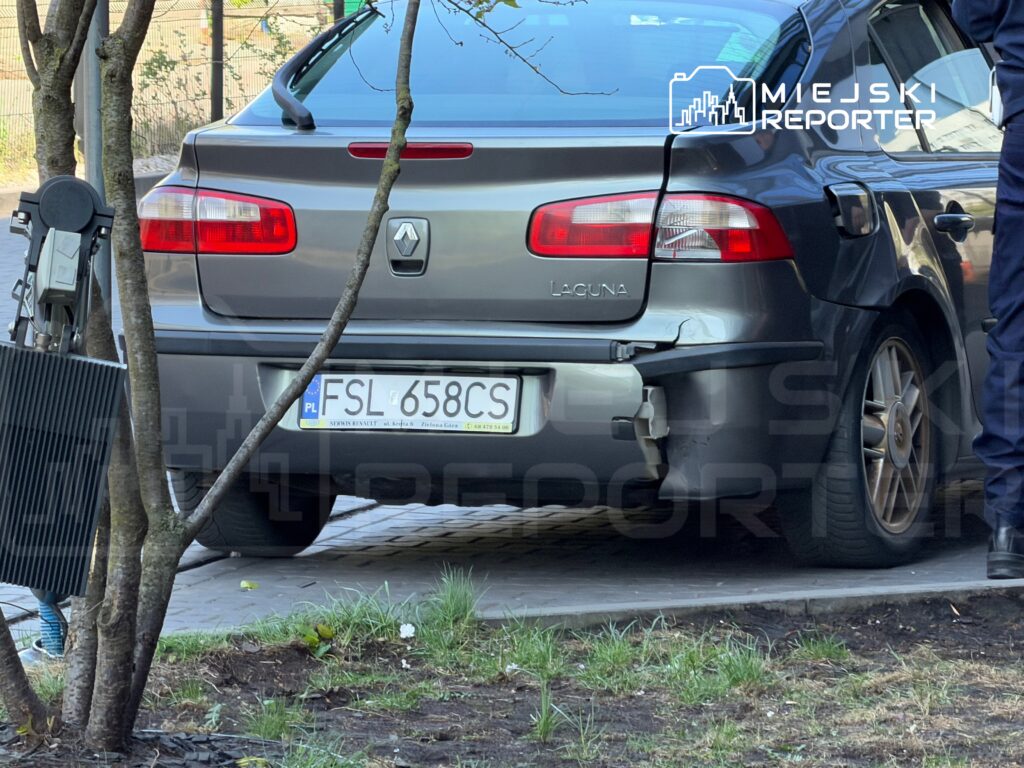 Uszkodzony samochód osobowy marki Renault Laguna zaparkowany na chodniku obok drzewa.