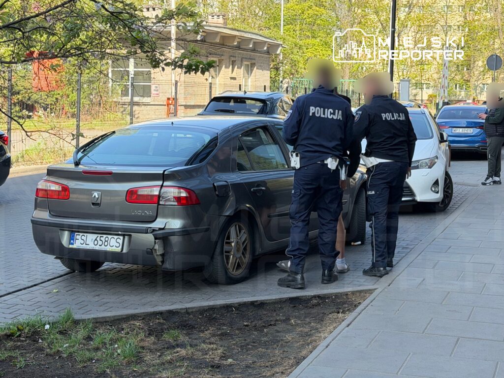 Dwaj policjanci rozmawiają z kierowcą stojącym obok uszkodzonego samochodu na ulicy.
