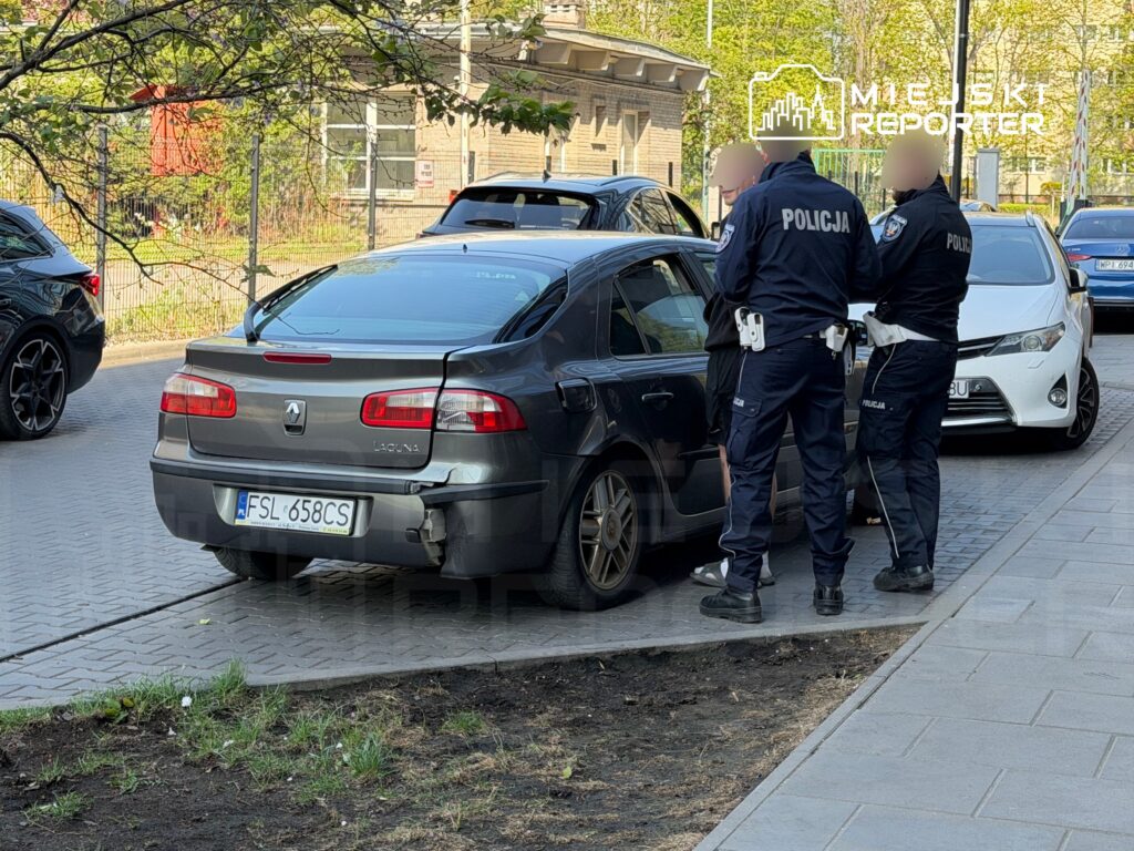 Dwaj policjanci rozmawiają z osobą stojącą obok uszkodzonego samochodu osobowego na chodniku.