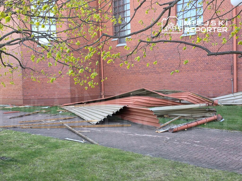 Zniszczona konstrukcja dachowa leży na trawniku obok czerwonej ceglanej ściany budynku.