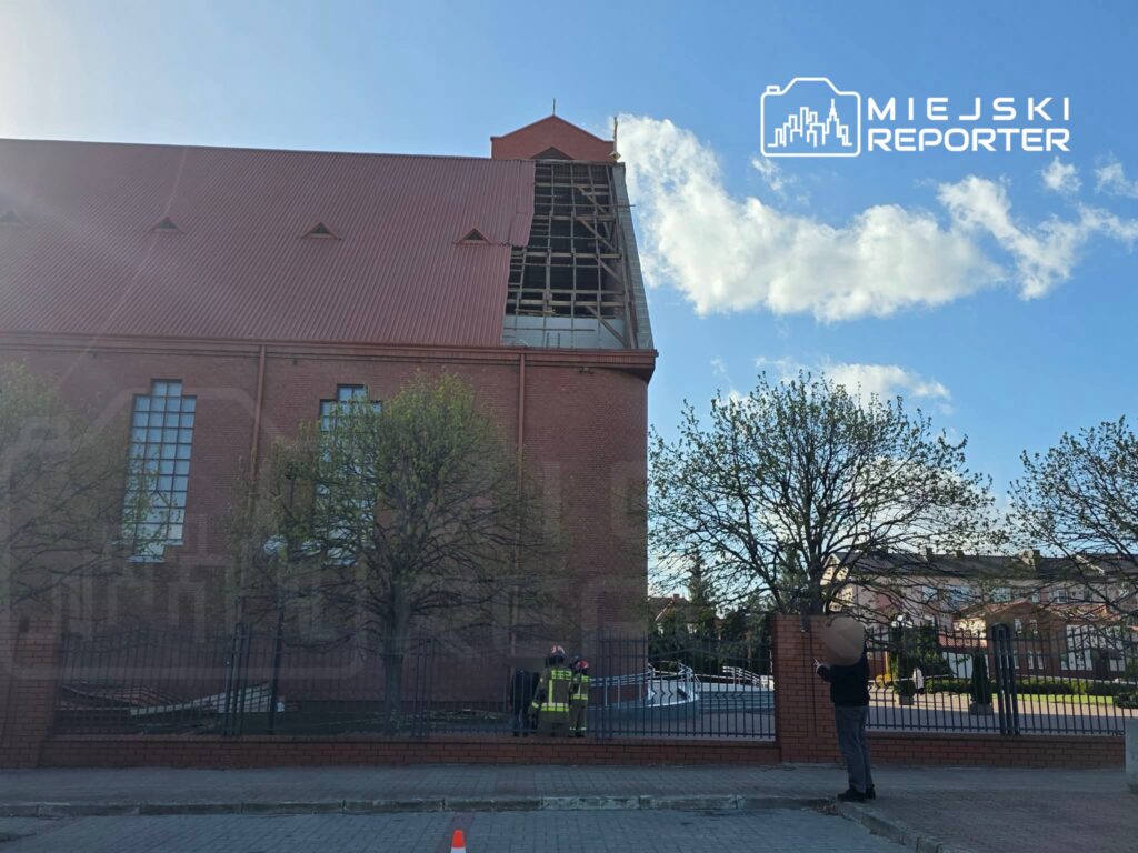 Pracownicy w kamizelkach odblaskowych oceniają uszkodzenia dachu budynku, otoczeni przez drzewa i chodnik.