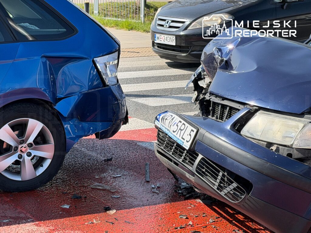 Dwa uszkodzone samochody osobowe na skrzyżowaniu, jeden z widocznymi wgnieceniami z tyłu, drugi z uszkodzoną maską.