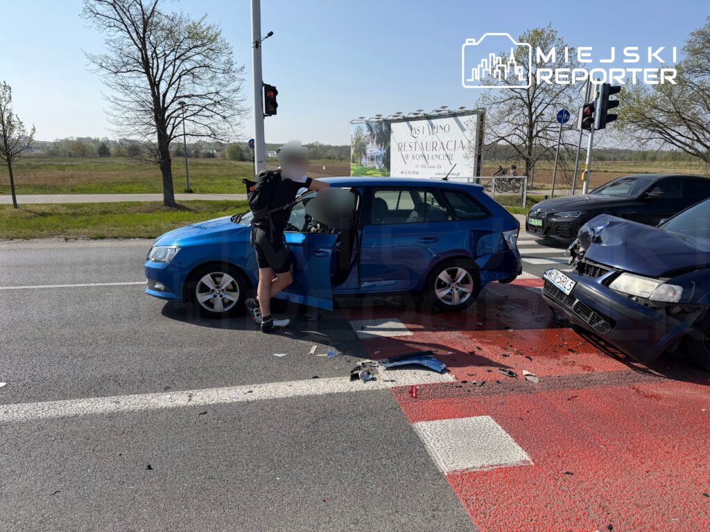 Kierowca w krótkich spodniach sprawdza uszkodzenia niebieskiego samochodu po kolizji na drodze, obok czerwonego światła.
