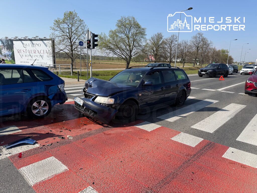 Dwa samochody osobowe zderzone na przejściu dla pieszych, w tle widać ruch uliczny i billboard reklamowy.