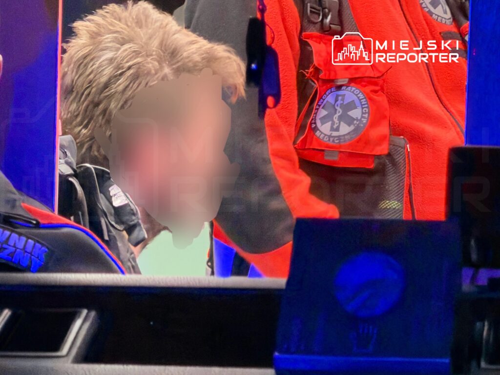 Ratownik medyczny udziela pomocy poszkodowanemu w karetce, otoczeni sprzętem medycznym i niebieskim światłem.