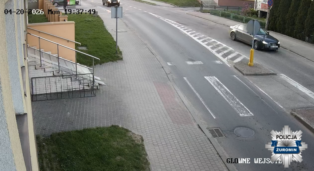 Samochód osobowy skręca w lewo na skrzyżowaniu obok schodów z poręczą wzdłuż chodnika.