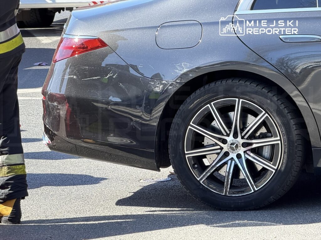 Uszkodzony samochód osobowy z wgniecioną karoserią na drodze, obok pracownik służb ratunkowych.