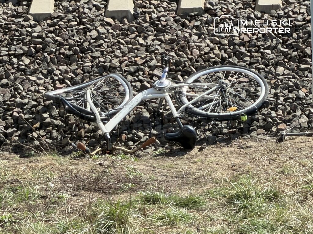 Zniszczony rower leży na kamienistym podłożu obok torów kolejowych.