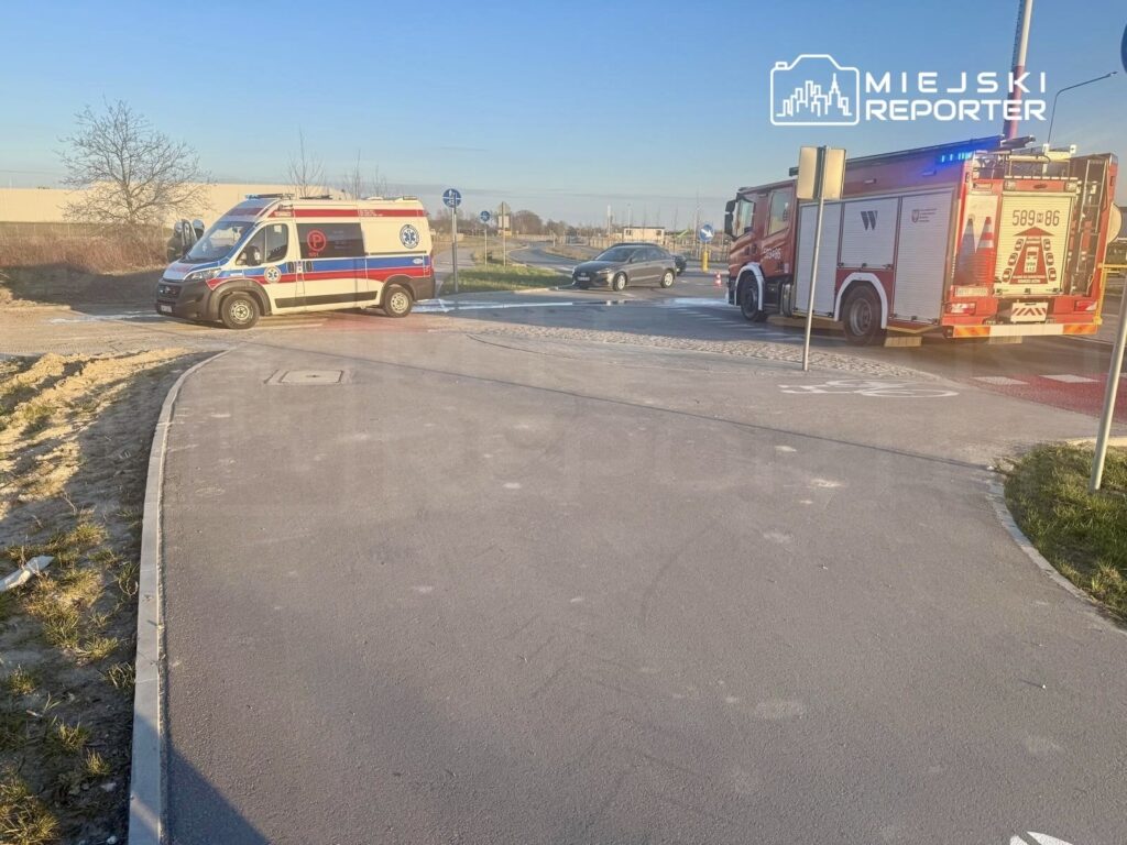 Ambulans i wóz strażacki zatrzymane na rondzie, obok widoczny samochód osobowy oraz znaki drogowe.