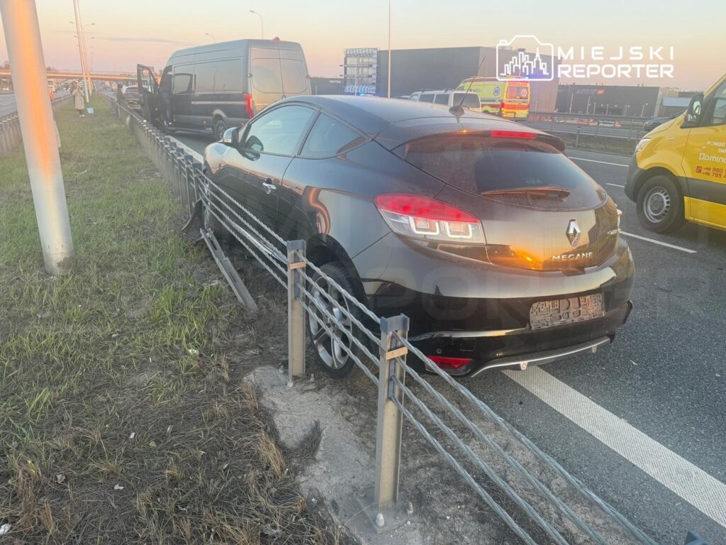 Czarny samochód osobowy marki Renault Megane zaparkowany na poboczu drogi, obok stoi furgonetka z otwartymi drzwiami.