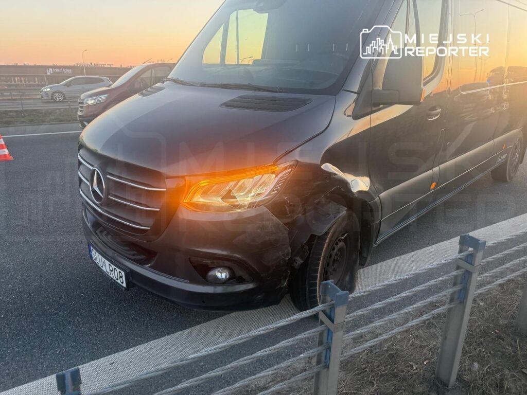 Czarny furgon marki Mercedes z uszkodzoną przednią częścią stoi na poboczu drogi w czasie zachodu słońca.