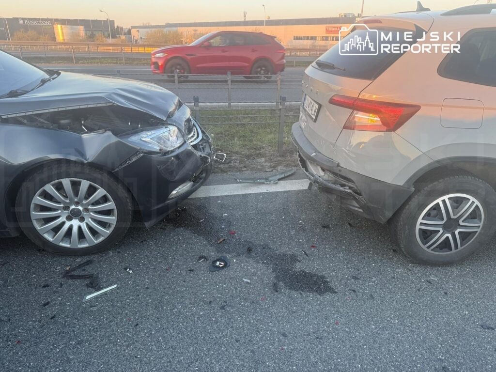 Dwa uszkodzone samochody osobowe stoją na poboczu drogi, obok leży rozbite szkło i fragmenty karoserii.