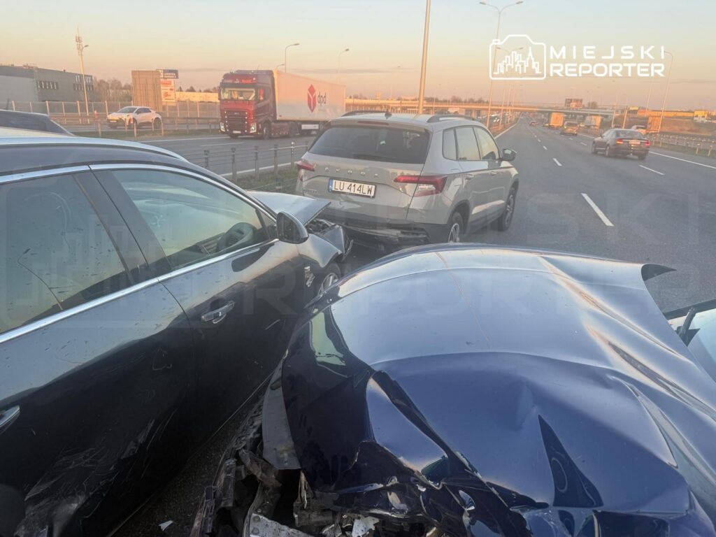 Zderzenie dwóch samochodów osobowych na pasie ruchu, w tle widoczny ruch innych pojazdów.