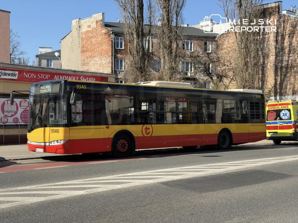 Autobus komunikacji miejskiej z numerem 9340 zatrzymany na przystanku obok ambulansu, w tle widoczne budynki.