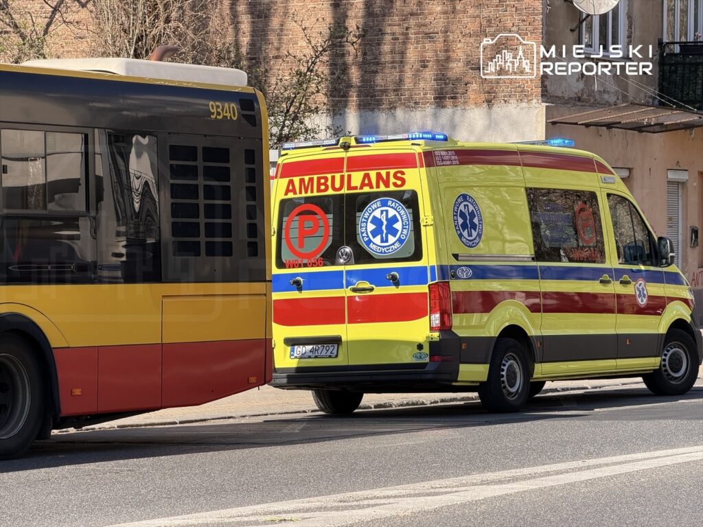 Karetka pogotowia z niebieskimi sygnałami stojąca obok miejskiego autobusu na ulicy.