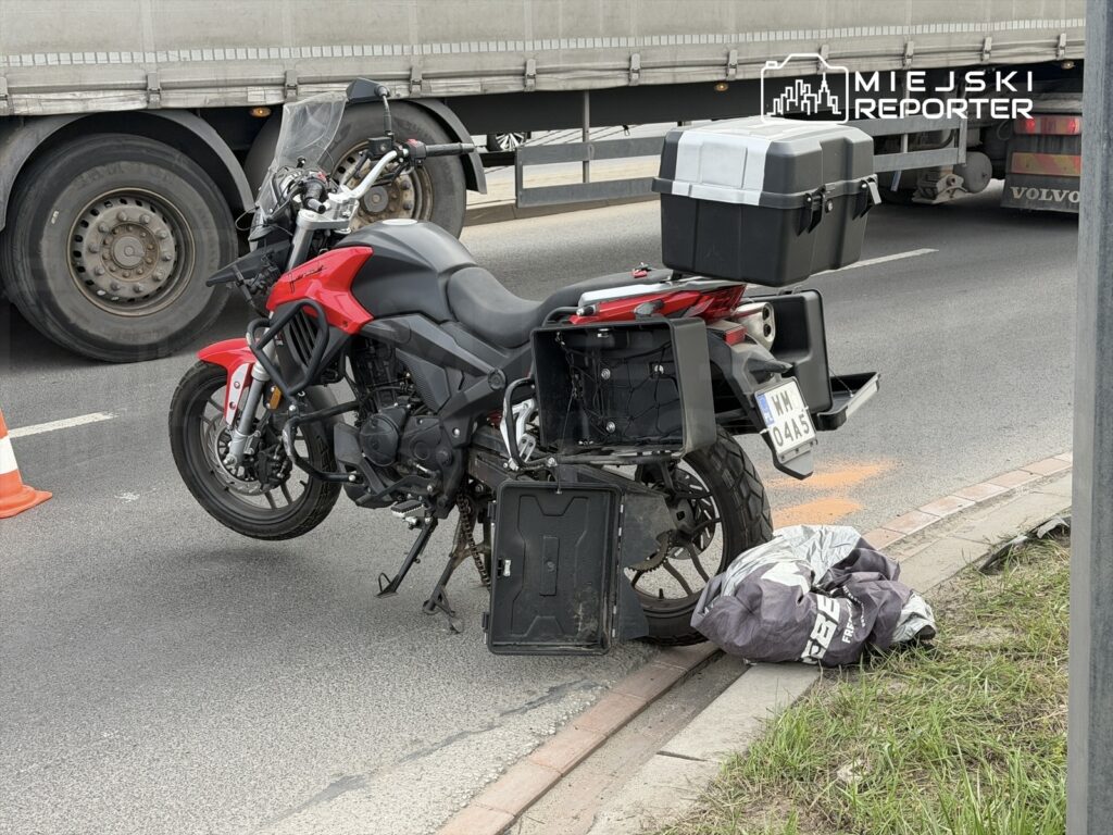 Motocykl z otwartymi bagażnikami stoi na poboczu drogi, w pobliżu dużego ciężarowego pojazdu.