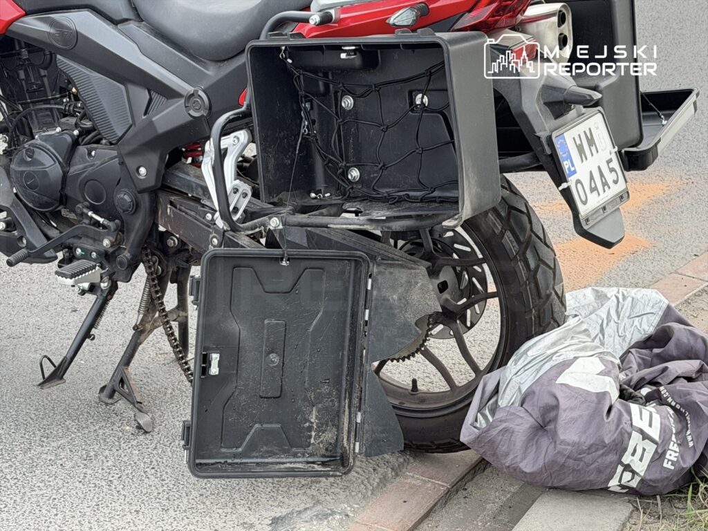 Motocykl z otwartą skrzynią bagażową stoi na ulicy obok złożonej osłony.