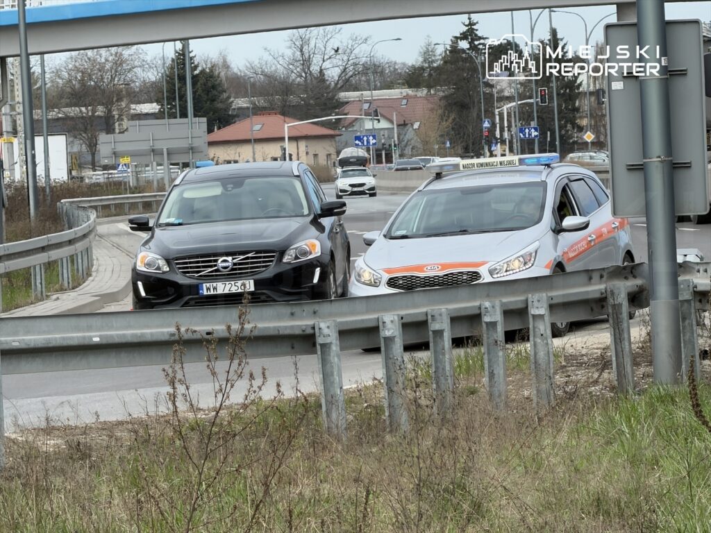 Czarny samochód osobowy zatrzymany obok szarego pojazdu służb drogowych na zakręcie drogi.
