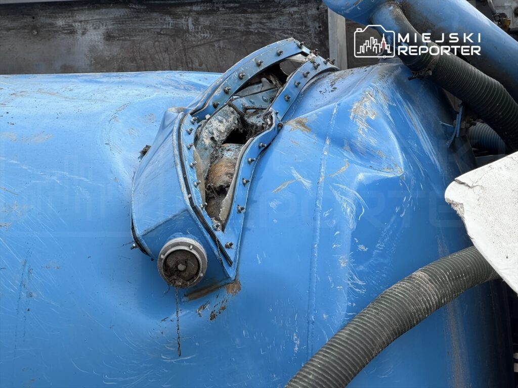 Uszkodzony element niebieskiej maszyny z widocznymi zarysowaniami i przerdzewiałymi częściami.