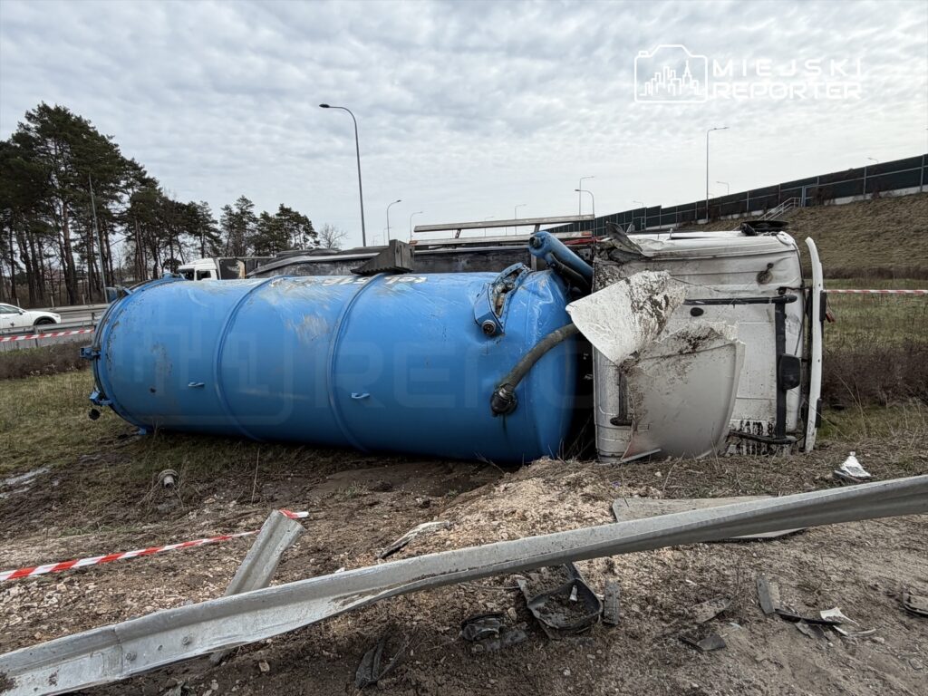 Niebieski zbiornik na ciężarówce leży na boku na poboczu drogi, otoczony taśmą ostrzegawczą.