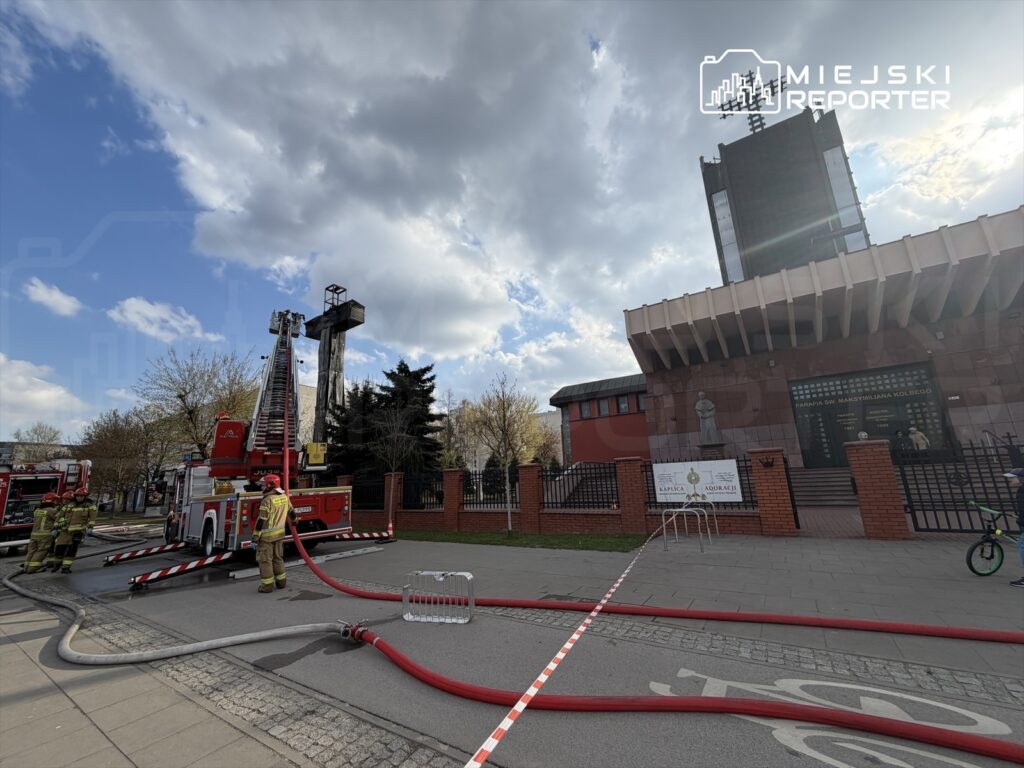 Strażacy obsługują węże strażackie obok wozu strażackiego w pobliżu budynku z przeszkloną fasadą.