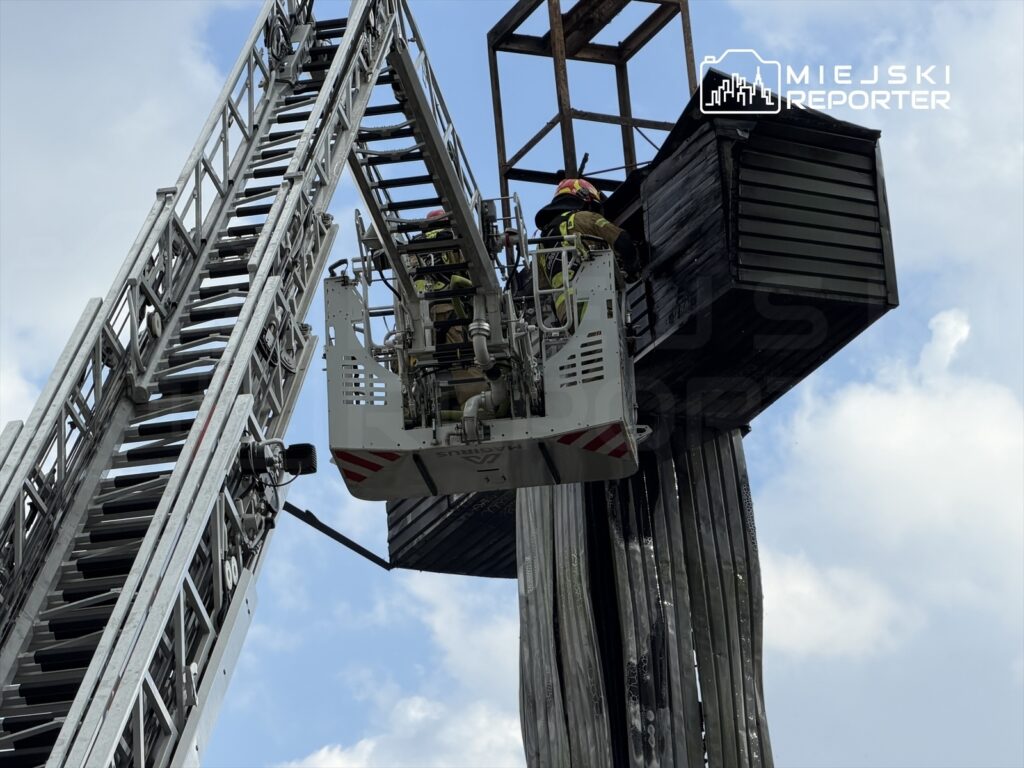 Strażacy w specjalnym podnośniku przeszukują zniszczony budynek z uszkodzoną elewacją pod chmurami.