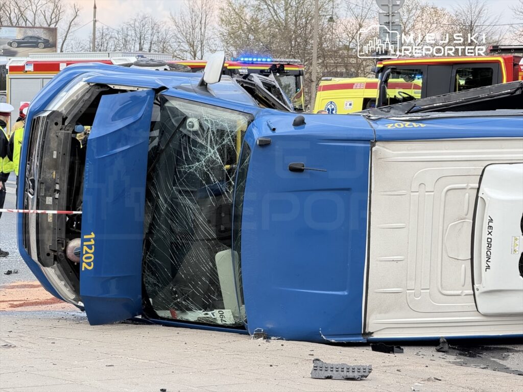 Niebieski pojazd osobowy leży na boku na jezdni, otoczony przez służby ratunkowe i policyjne.