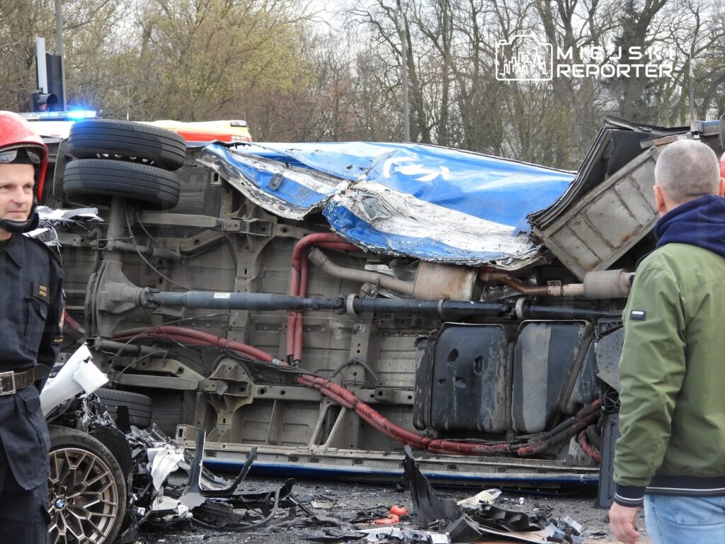 Ratownicy przy wypadku drogowym, gdzie przewrócony pojazd leży na boku, a wokół rozrzucone szczątki.