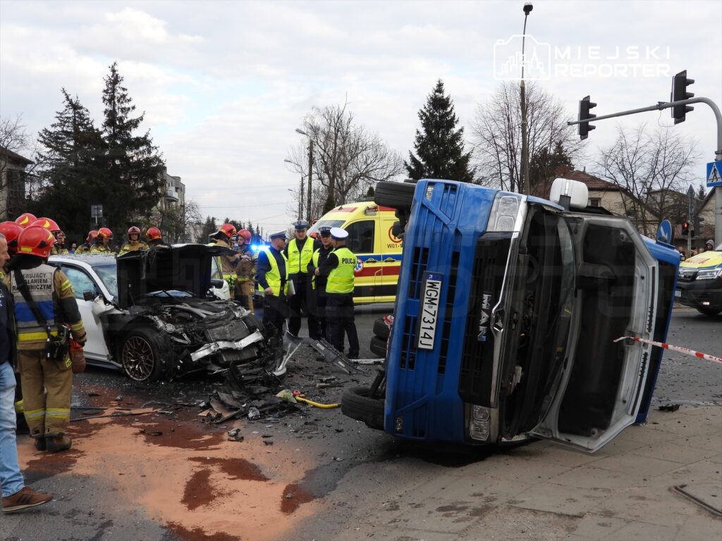 Ratownicy i policjanci pracują przy wypadku drogowym, gdzie samochód osobowy zderzył się z przewróconą ciężarówką.
