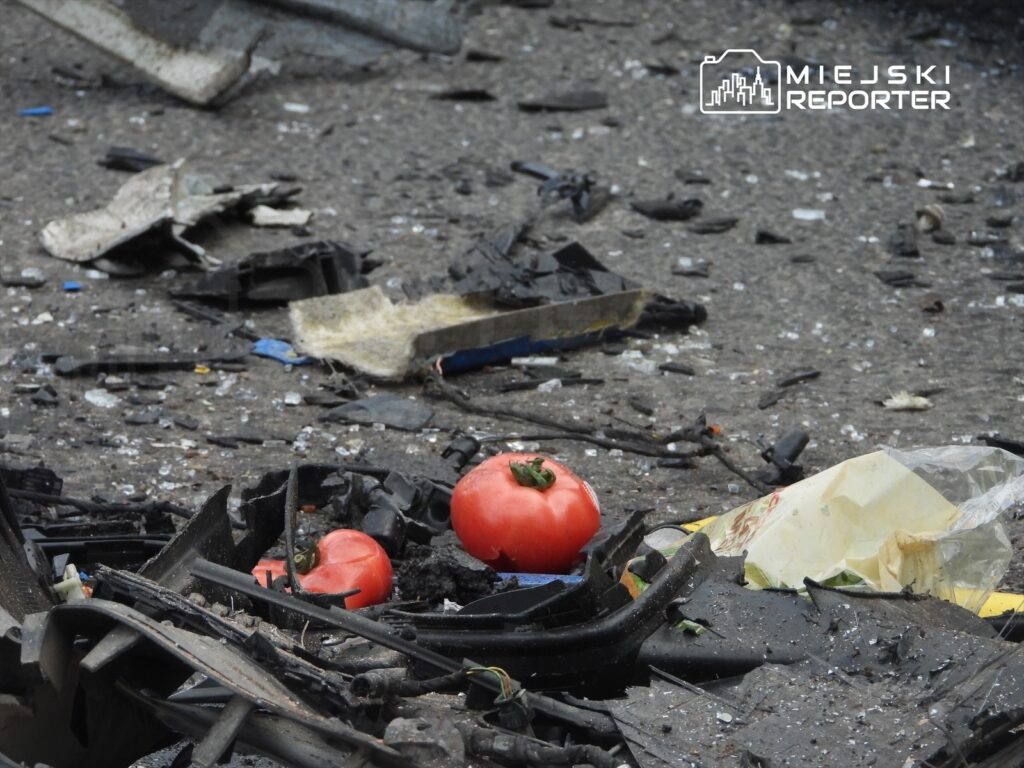 Czerwone pomidory leżą na zniszczonym asfalcie wśród odpadków i fragmentów plastikowych.