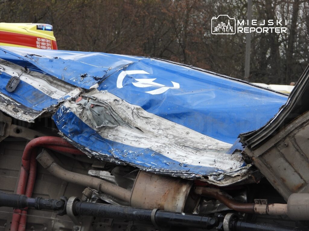 Uszkodzony pojazd z niebieską karoserią leżący na boku, odsłaniający uszkodzenia metalowych elementów.