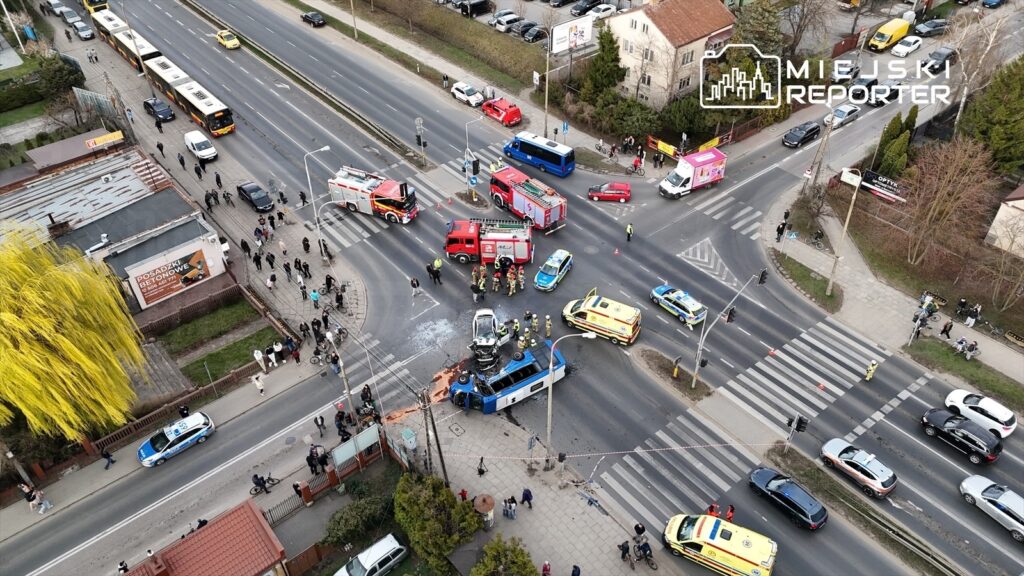 Wielka kolizja drogowa z udziałem samochodów osobowych i pojazdów służb ratunkowych na skrzyżowaniu.