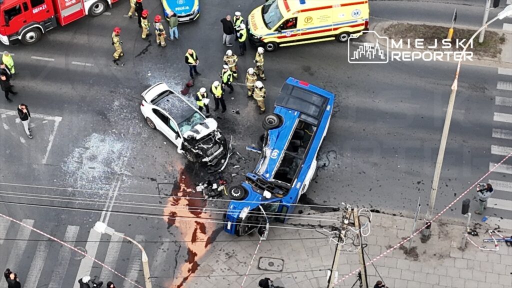 Wielu ratowników i policjantów pracuje przy wypadku drogowym, gdzie przewrócony autobus zderzył się z osobowym samochodem.